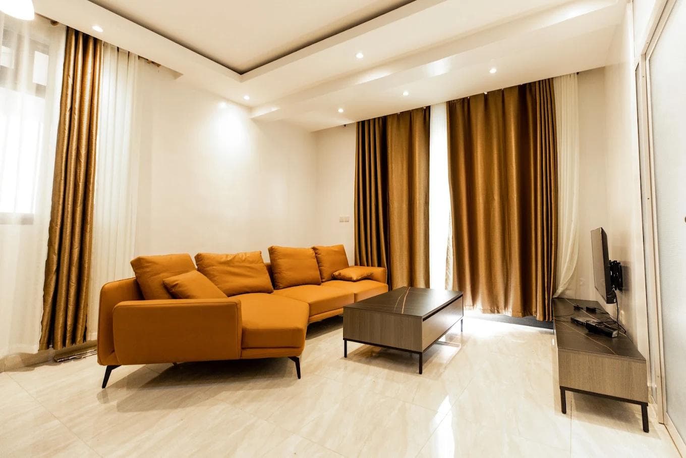 Living room of a two-bedroom serviced apartment at Laurus Apartments, Kigali, with a corner sofa and floor-to-ceiling curtains